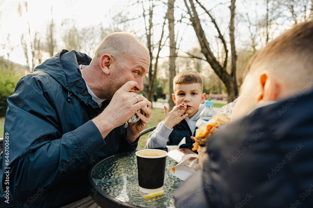 Father with his two little sons having a snack in outdoor cafe Father with his two little sons having a snack in outdoor cafe