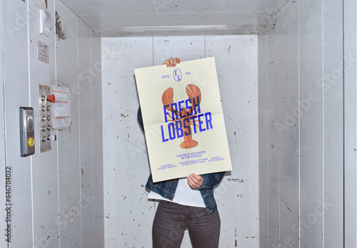 Mockup of woman holding customizable A2 vertical poster in front of face in elevator, camera flash