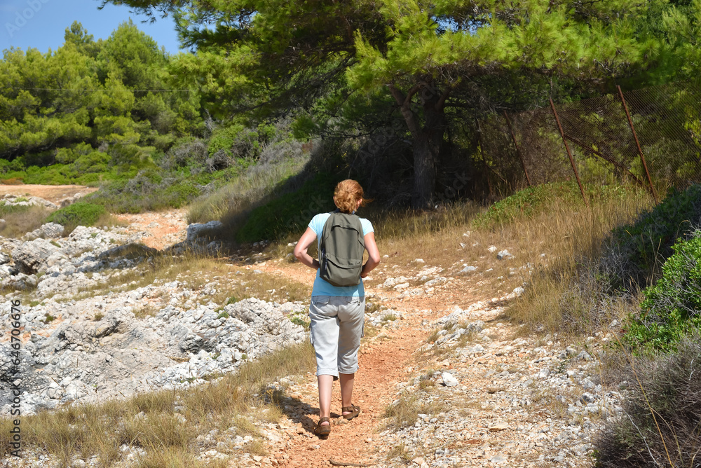 Woman with backpack walking on the coastal path near the sea and enjoying the nature. Back view. Travel and active lifestyle concept. Woman with backpack walking on the coastal path near the sea and enjoying the nature. Back view. Travel and active lifestyle concept.