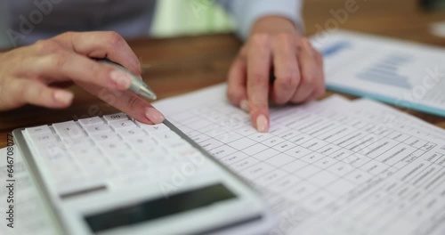 Female hand of marketer or accountant holds pen and presses numbers on acalculator and checks report. Financial statistics and report photo