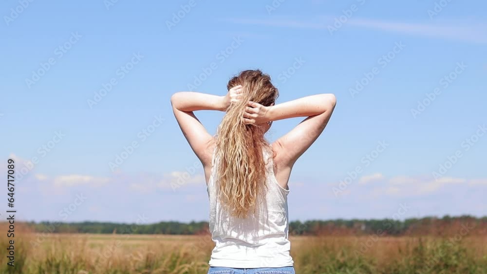 The girl on the background of the field and the blue sky, rear view. Summer blue sky, open space, tourism or allergy freedom concept. A beautiful girl with long hair breathes fresh air The girl on the background of the field and the blue sky, rear view. Summer blue sky, open space, tourism or allergy freedom concept. A beautiful girl with long hair breathes fresh air