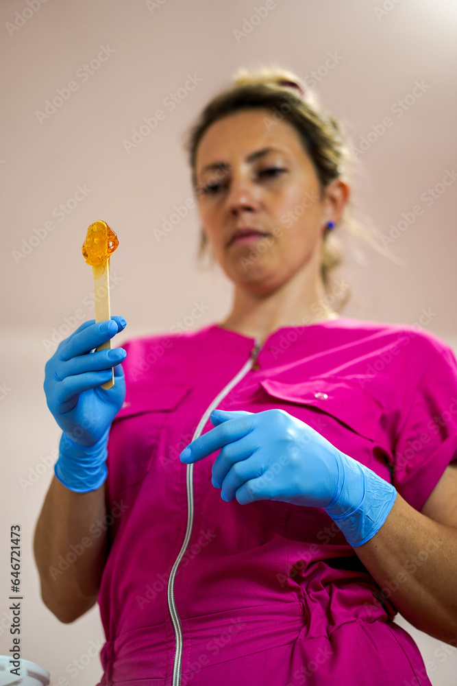 Portrait of hair removal master in gloves holds a wooden stick with sugar paste. Sugaring salon Portrait of hair removal master in gloves holds a wooden stick with sugar paste. Sugaring salon