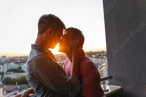 Obraz na płótnie A young gay couple in love standing on a balcony overlooking the city at sunset