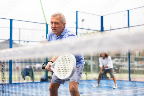 View through the tennis net at an elderly player in the game of padel