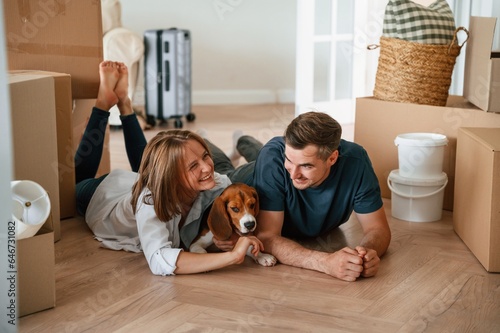Happy young couple with dog are moving to new home. On the floor