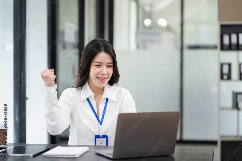 Smiling young asian woman succeeding in business using laptop and computer while doing some paperwork at office. Smiling young asian woman succeeding in business using laptop and computer while doing some paperwork at office.