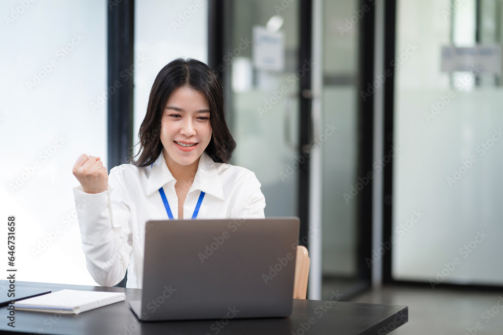 Smiling young asian woman succeeding in business using laptop and computer while doing some paperwork at office. Smiling young asian woman succeeding in business using laptop and computer while doing some paperwork at office.