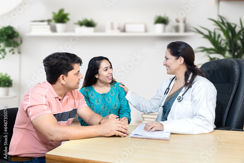 Indian female gynecologist doctor consulting young married couple patients in fertility clinic about IVF or IUI. Planning pregnancy concept.