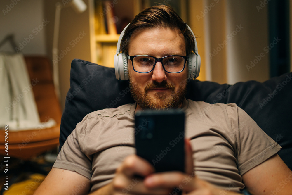 Adult man with glasses plays music on his phone and listens trough headphones. Adult man with glasses plays music on his phone and listens trough headphones.