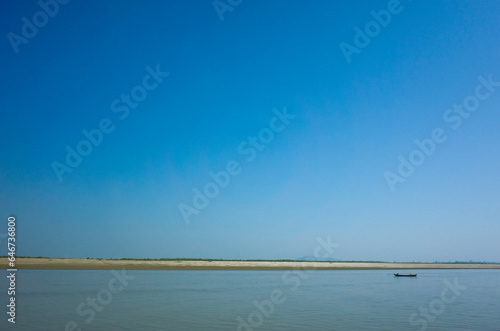 River landscape. Thin coast line divides clear blue sky and blue river  small boat on Irrawaddy river near Mandalay  Myanmar