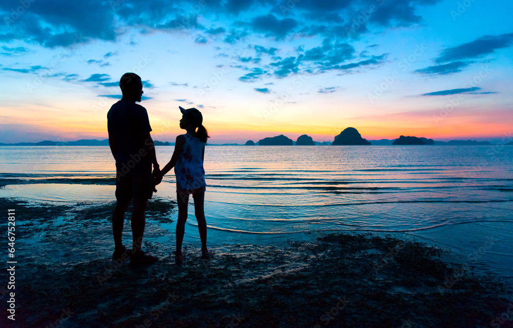 Silhouette Asian father and teenage daughter holding hands talking, standing together on sunset beach. Daddy and child girl hand in hand. Fathers day concept, Tub Kaek beach,Krabi,Thailand. Copy space