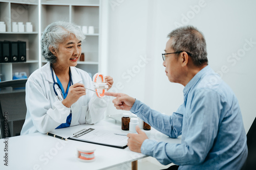 Concentrated dentist sitting at table with jaw samples tooth model and working with tablet and laptop in dental office professional dental clinic.