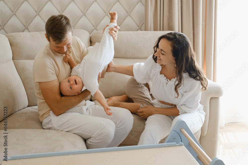 Family with two kids on the couch having fun. Mather, father baby and toddler sons are happy in the morning in Livingroom. Children playing with parents at home. Real life and quality time Family with two kids on the couch having fun. Mather, father baby and toddler sons are happy in the morning in Livingroom. Children playing with parents at home. Real life and quality time