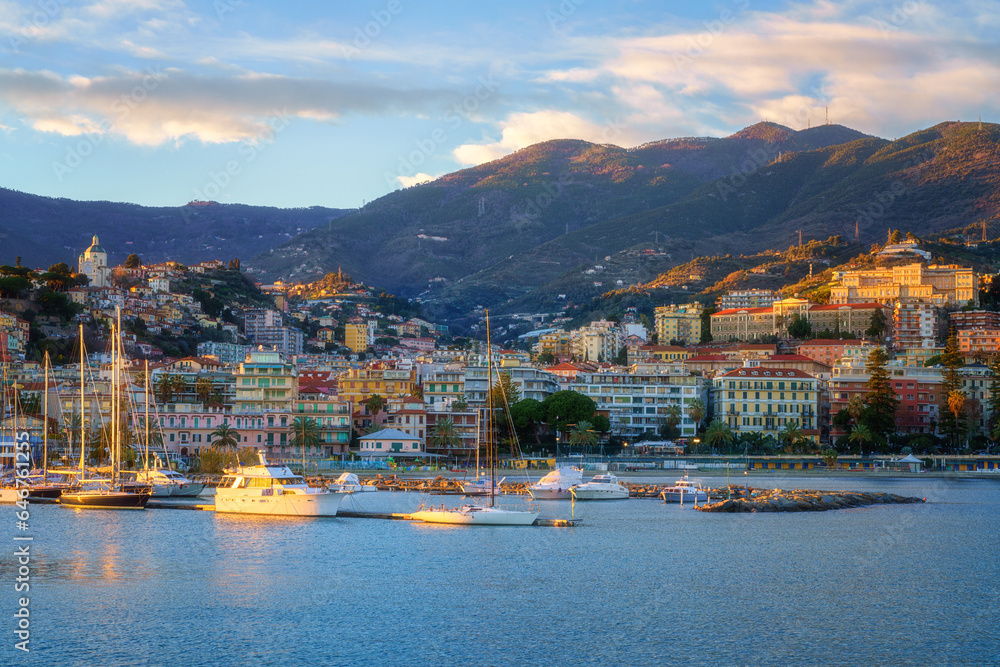 Panoramic view of Sanremo or San Remo from the sea, Italian Riviera, Liguria, Italy. Scenic sunset landscape with city architecture, seafront, mountains, blue water and sky, outdoor travel background