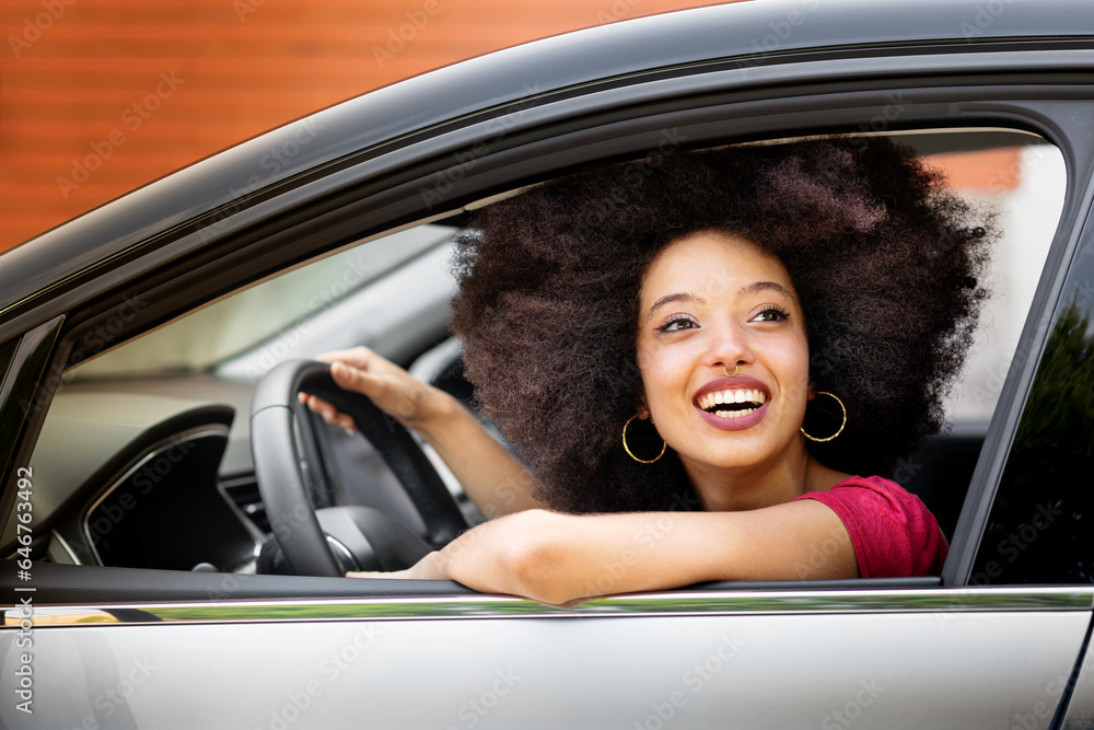 Happy young black woman sitting in driver seat of car in daylight