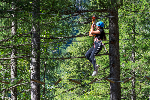 Happy young woman in helmet walking on ropes in forest park in daylight