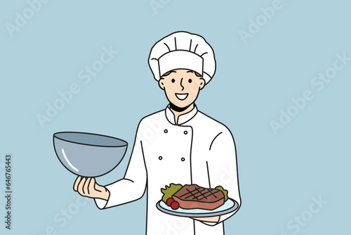 Man chef holds tray with beef steak and vegetables, inviting you to visit restaurant of classic european cuisine. Guy in cook uniform demonstrates grilled pork steak at popular steakhouse.