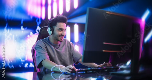 Portrait of a Happy Young Man in Headphones Talking with Friends Online on a Computer. Stylish Streamer or Video Gamer Playing Games and Chatting with Internet Followers in a Futuristic Neon Studio