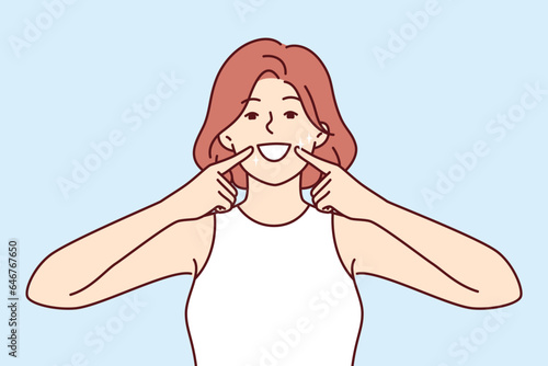 Woman smile and shows off white teeth and points fingers at mouth to invite people to dental clinic. Positive girl is trained to make big smile to appear friendly for successful sales