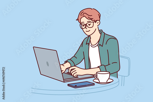 Man freelancer works with laptop sitting in cafe and drinking coffee enjoying remote work as programmer. Freelancer guy uses portable computer to create website or mobile app for phone