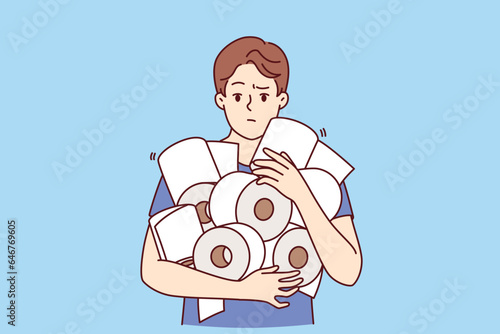 Man holds pile of toilet paper in hands, having experienced panic due to announcement of storm warning or quarantine. Funny guy with toilet paper for concept of shortage of hygiene products in store photo