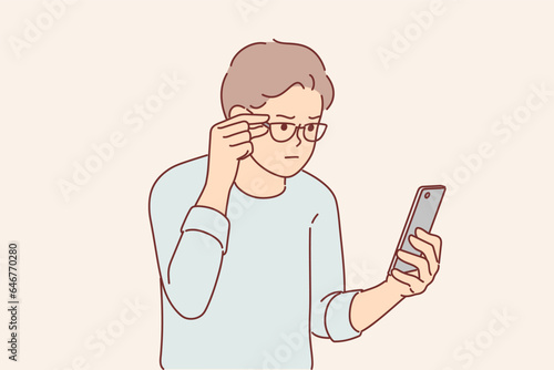 Man has vision problems and reads SMS message in small print on phone, adjusting glasses on eyes