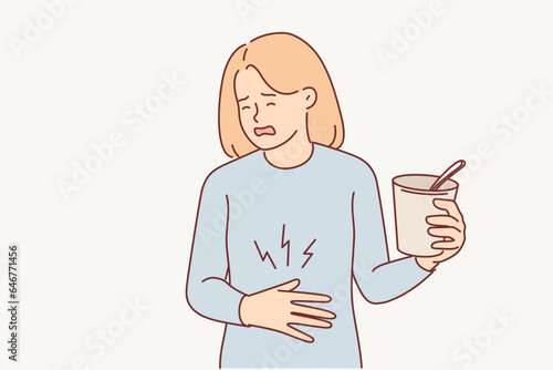 Woman suffers from heartburn and puts hand on stomach, holding glass of ice cream or instant soup