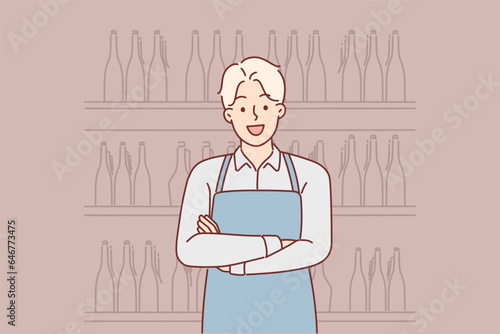 Man works in winery standing with crossed arms near racks filled with bottles of wine