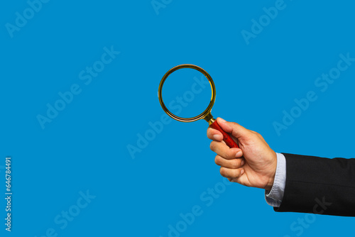 Businessman in a suit is holding a magnifier on a blue background