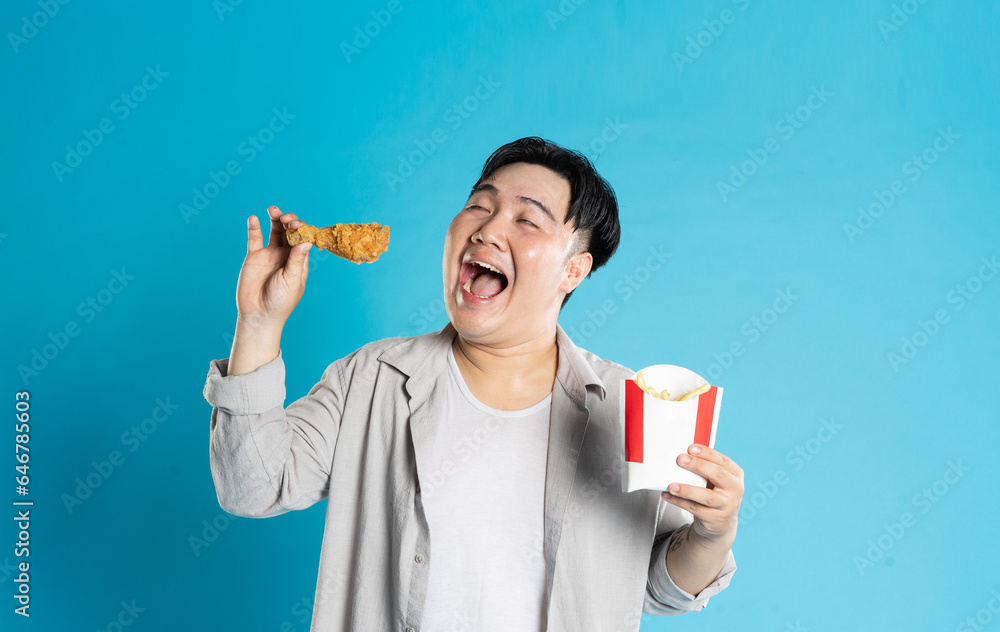 Portrait of asian man eating fast food on blue background Portrait of asian man eating fast food on blue background