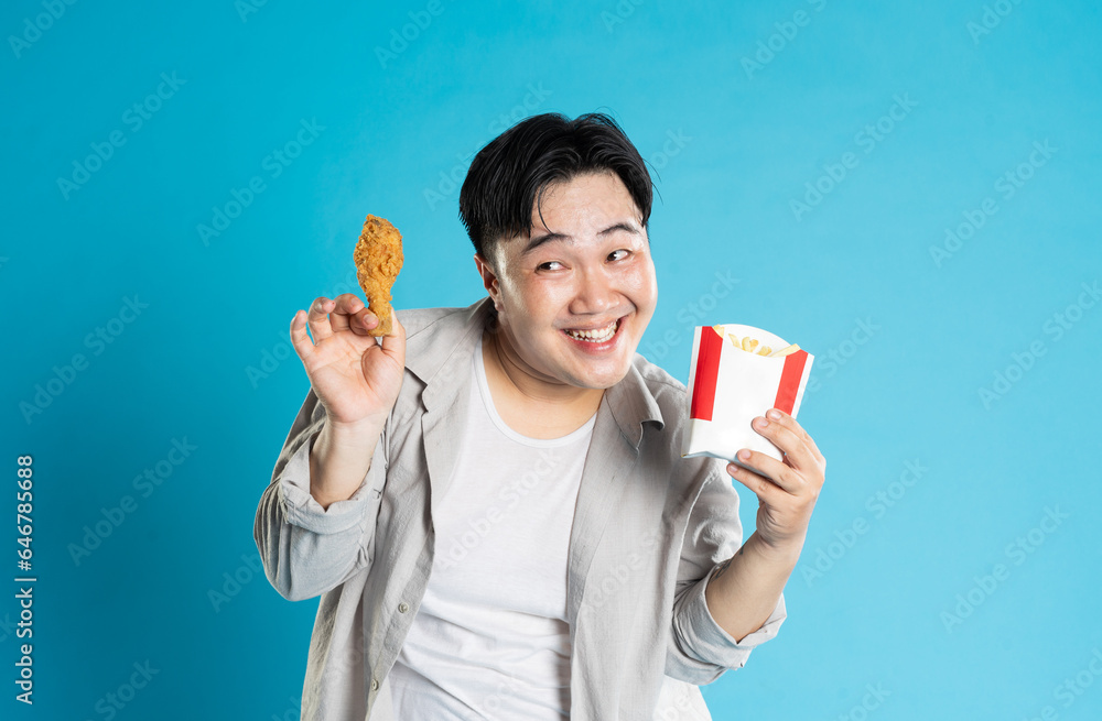 Portrait of asian man eating fast food on blue background Portrait of asian man eating fast food on blue background
