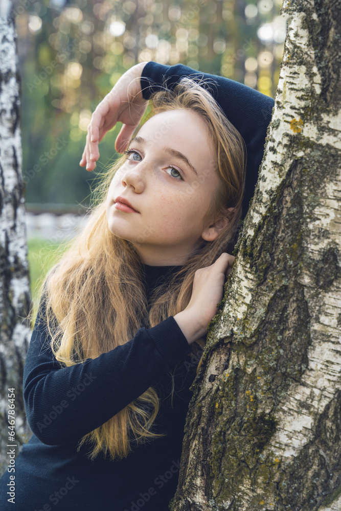 Close-up portrait of a romantic 13-15 year old girl in the woods. A girl with long blond hair looks at the camera