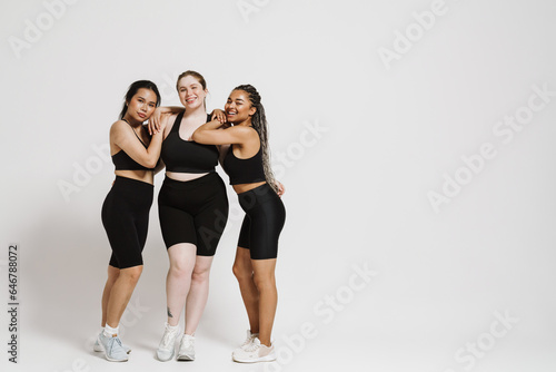 Three smiling women with different body types posing together isolated over white background