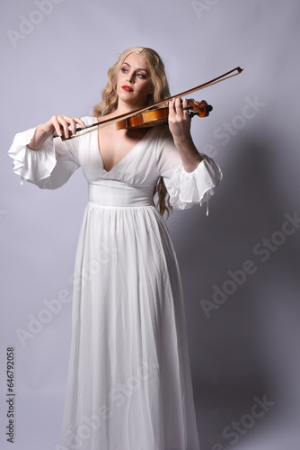 Close up portrait of beautiful blonde model wearing elegant white halloween gown, a historical fantasy character. Holding a violin musical instrument, isolated on studio background.