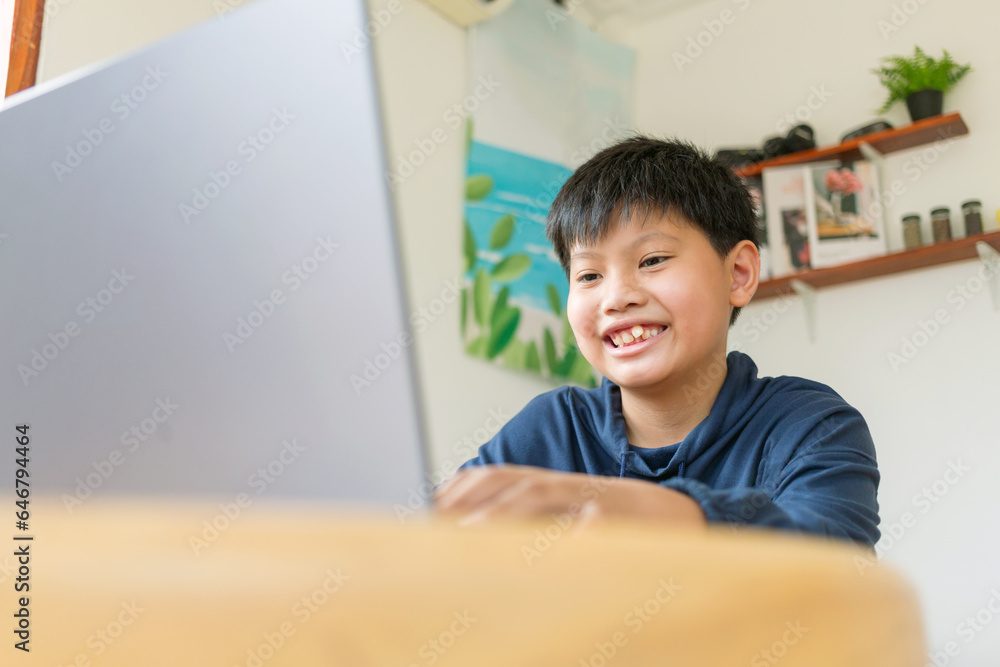 Smiling Asian kids boy chatting with friends or a student studying the internet on social networks sitting in a front laptop at home. Chat on Social Media and video conference. Smiling Asian kids boy chatting with friends or a student studying the internet on social networks sitting in a front laptop at home. Chat on Social Media and video conference.