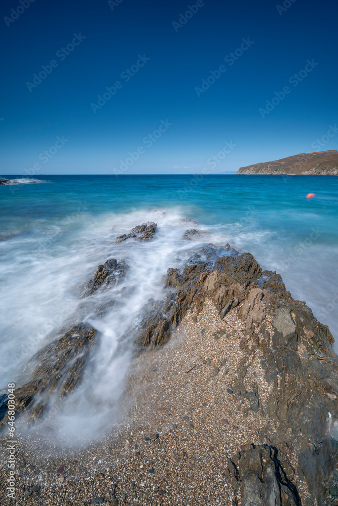 clear blue sky and waves crashing on rocks shot blurry