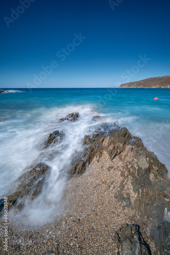 clear blue sky and waves crashing on rocks shot blurry