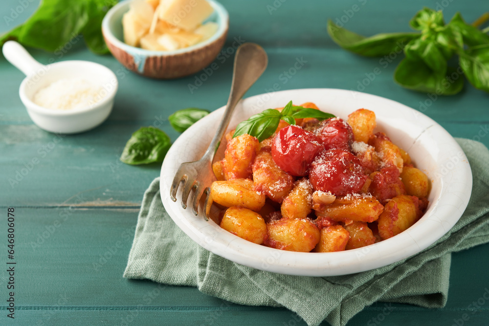 Potato gnocchi. Traditional homemade potato gnocchi with tomato sauce, basil and parmesan cheese on turquoise rustic kitchen table background. Traditional Italian food. Top view. Potato gnocchi. Traditional homemade potato gnocchi with tomato sauce, basil and parmesan cheese on turquoise rustic kitchen table background. Traditional Italian food. Top view.