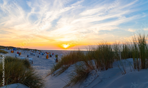 Beach and sand dune panorama at sunset on Juist island  North Sea Germany. Calm warm atmosphere with colorful beach chairs  grass and sea on the horizon. Popular holiday destination in National park.