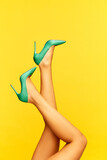 Female slender legs wearing stylish, heeled, green shoes with animal print over bright yellow background. Romantic. Colorful photography. Concept of fashion, creativity, imagination. Copy space for ad
