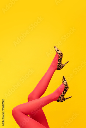 Female slender legs wearing stylish, heeled shoes with animal print and red tights over bright yellow background. Colorful photography. Concept of fashion, creativity, imagination. Copy space for ad