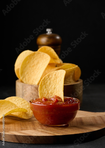 Potato chips in a wooden bowl and a bowl of sauce on a black table, snack photo