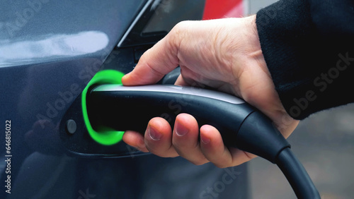 close-up view of hand holding an electric vehicle charging gun connector and plugging it into charger port of electric car. EV charge process parts concept background.