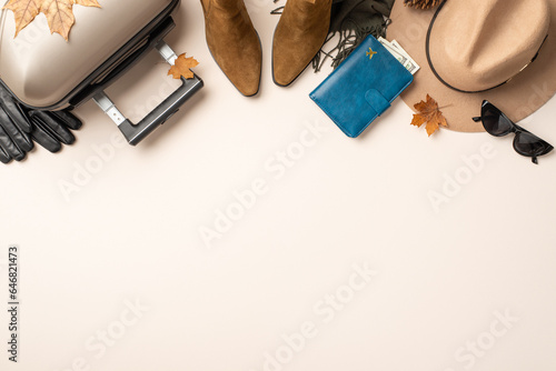 Feminine autumn travel vibes: top-view shot of essentials - felt hat, cat-eye sunglasses, scarf, ankle boots, gloves, suitcase, purse, leaves, and pine cone on a neutral canvas with blank space for ad