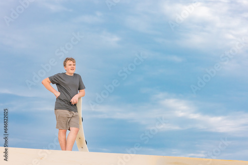Boy standing on sand dune holding sand board on Stockton Beach photo