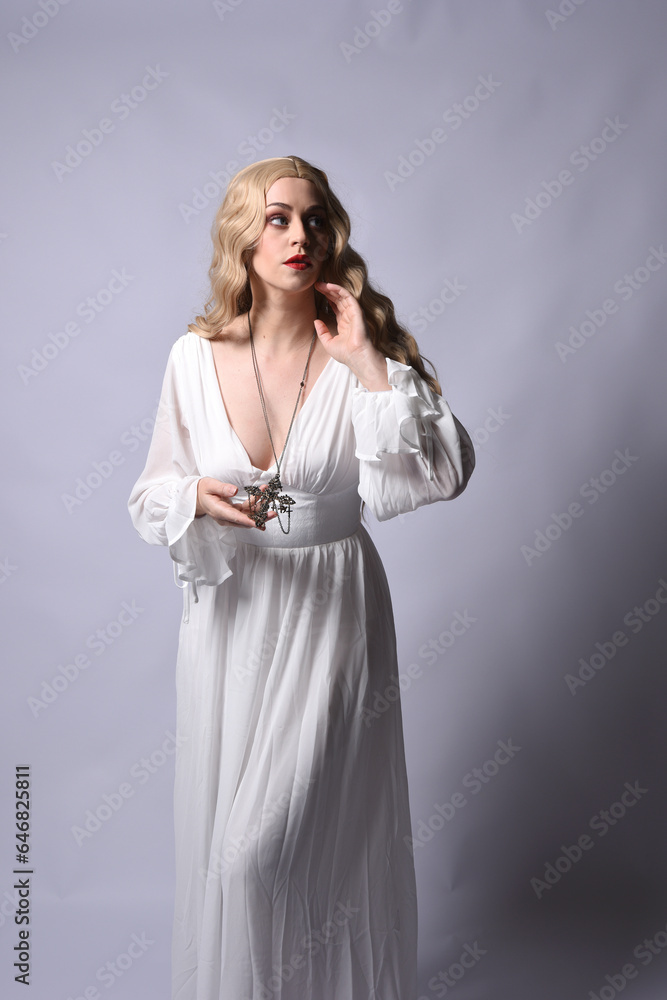 Close up portrait of beautiful blonde model wearing elegant white halloween gown, a historical fantasy character. Holding crucifix cross necklace, isolated on studio background. Close up portrait of beautiful blonde model wearing elegant white halloween gown, a historical fantasy character. Holding crucifix cross necklace, isolated on studio background.