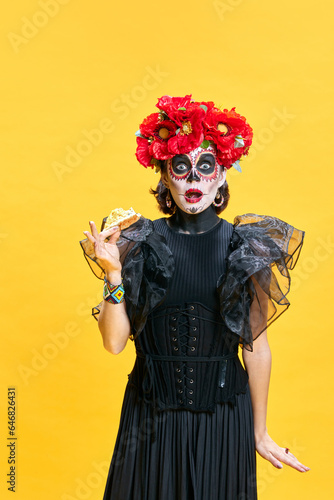 Young surprised woman in spooky makeup eating delicious hot pizza against bright yellow background. Concept of holiday, party, Halloween