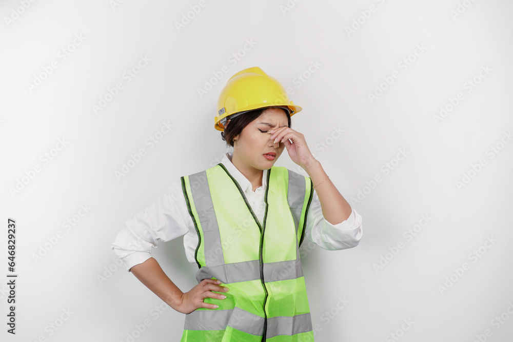 A portrait of Asian woman labor wears safety helmet and vest, looks stressed and depressed, isolated white background.