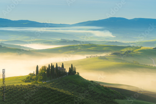 House surrounded by cypress trees among the misty morning sun-drenched hills of the Val d Orcia valley at sunrise in San Quirico d Orcia  Tuscany  Italy