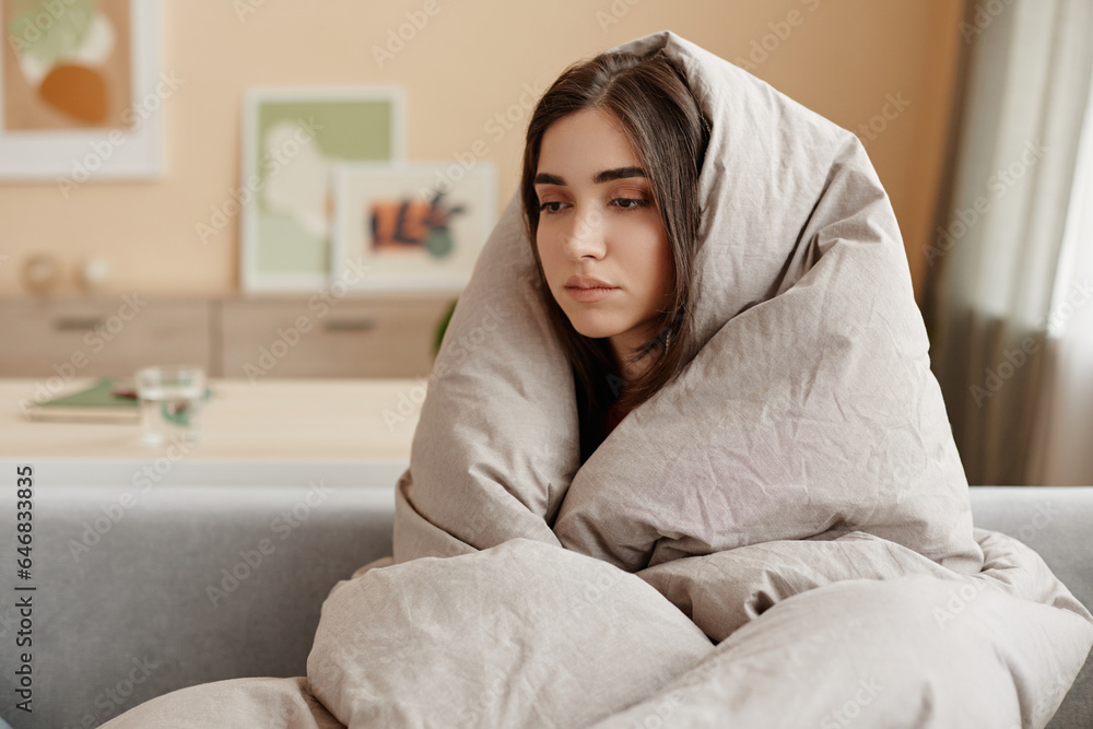 Portrait of depressed young woman wrapped in blankets at home struggling with mental health issues, copy space Portrait of depressed young woman wrapped in blankets at home struggling with mental health issues, copy space